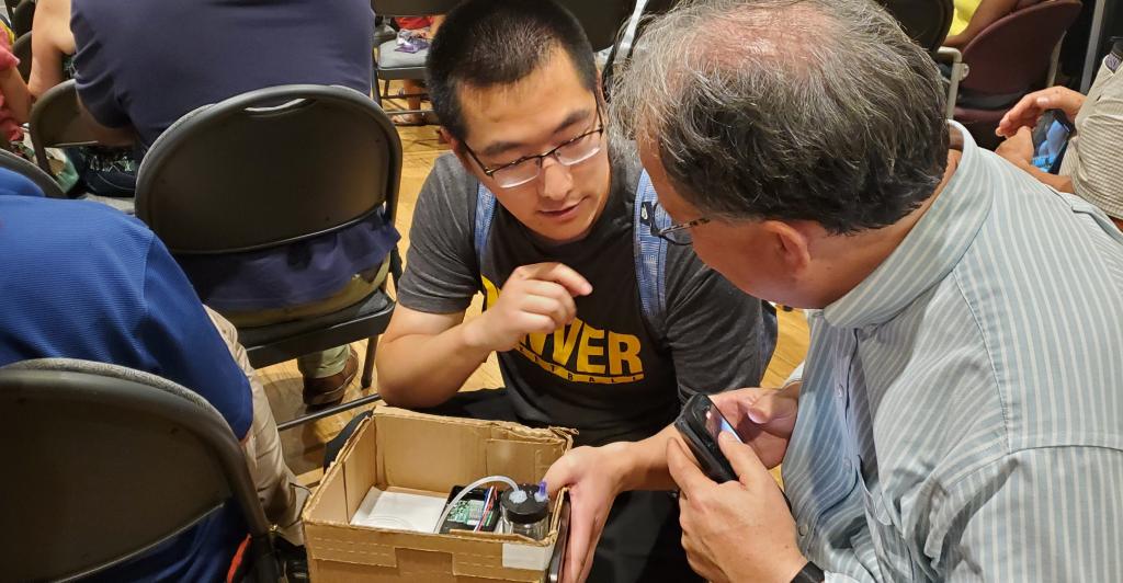 Yajing crouching and holding box with sensor in it while speaking to another person